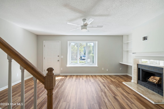 unfurnished living room with light hardwood / wood-style flooring, a textured ceiling, a tile fireplace, and ceiling fan