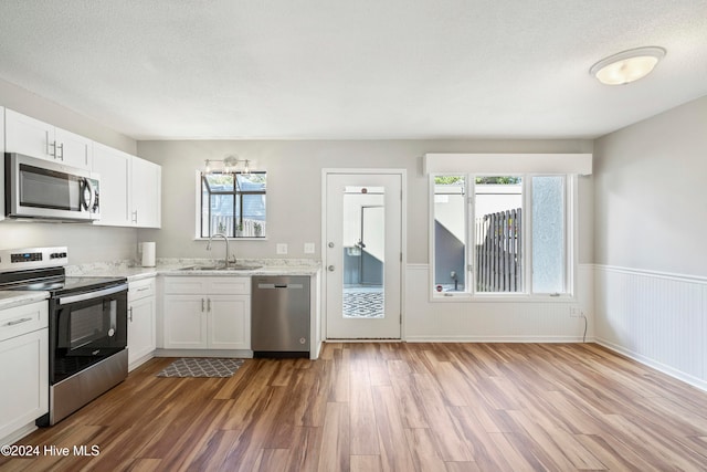 kitchen with hardwood / wood-style floors, white cabinets, appliances with stainless steel finishes, a textured ceiling, and sink