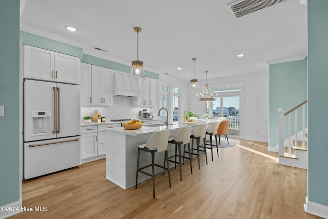 kitchen featuring white cabinetry, premium range hood, light hardwood / wood-style floors, high end white fridge, and a kitchen island with sink