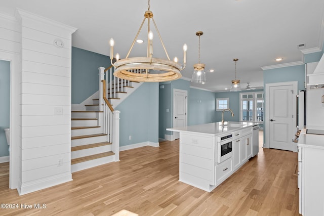 kitchen featuring sink, an island with sink, pendant lighting, light hardwood / wood-style floors, and ornamental molding