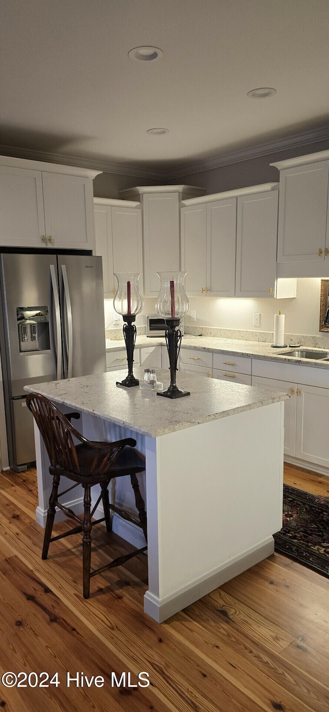 kitchen with white cabinets, light stone counters, stainless steel fridge with ice dispenser, hardwood / wood-style flooring, and a center island