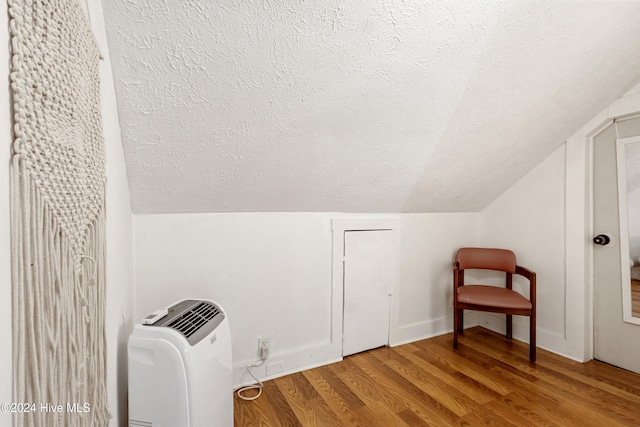 additional living space with wood-type flooring, a textured ceiling, and vaulted ceiling