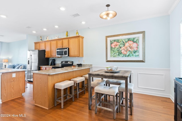 kitchen with decorative light fixtures, kitchen peninsula, crown molding, light wood-type flooring, and stainless steel appliances