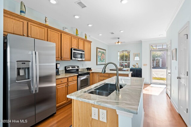 kitchen with stainless steel appliances, an island with sink, light hardwood / wood-style floors, sink, and light stone counters