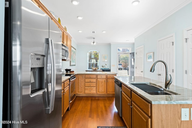 kitchen featuring a center island with sink, wood-type flooring, sink, ornamental molding, and stainless steel appliances