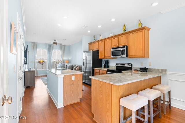 kitchen featuring a kitchen bar, stainless steel appliances, sink, kitchen peninsula, and ceiling fan