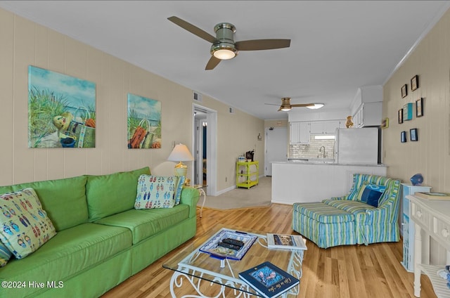 living room with ornamental molding, sink, light wood-type flooring, and ceiling fan