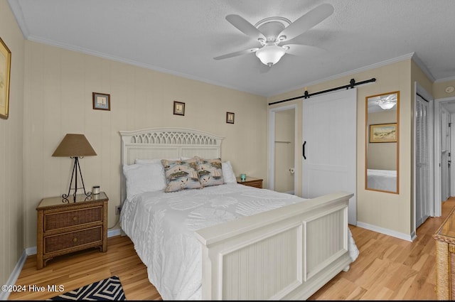 bedroom featuring hardwood / wood-style flooring, a closet, crown molding, a barn door, and ceiling fan