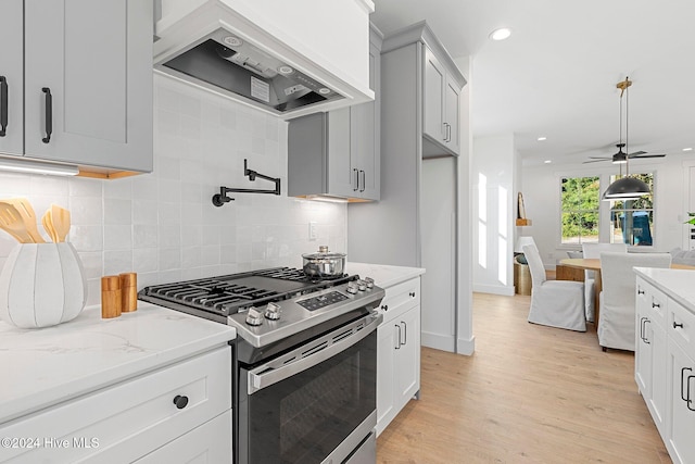 kitchen with gas stove, backsplash, light stone countertops, custom range hood, and light hardwood / wood-style floors