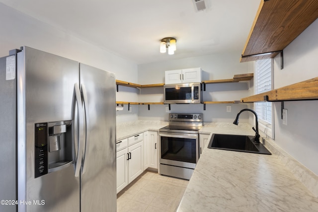 kitchen with stainless steel appliances, light tile patterned floors, sink, light stone countertops, and white cabinetry