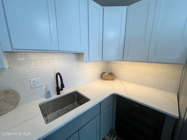 kitchen featuring light stone countertops, backsplash, blue cabinets, white cabinets, and sink