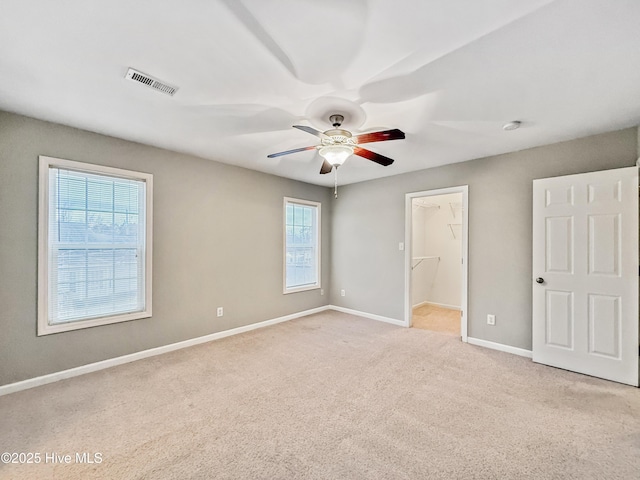 unfurnished bedroom with ceiling fan, a walk in closet, light carpet, and a closet