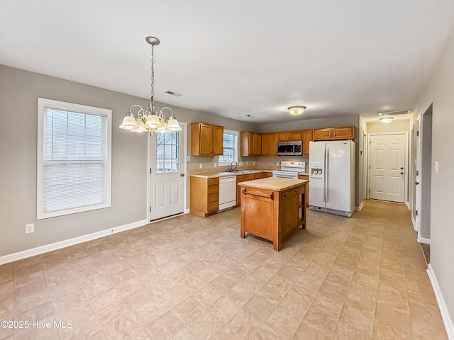 kitchen with sink, an inviting chandelier, a center island, hanging light fixtures, and white appliances