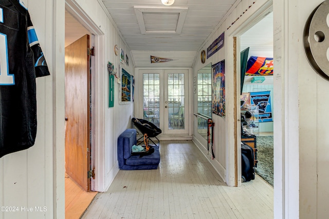 hallway featuring light hardwood / wood-style flooring, french doors, wooden walls, and vaulted ceiling