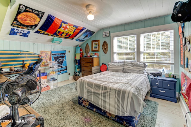 bedroom featuring light hardwood / wood-style flooring, wooden walls, and vaulted ceiling