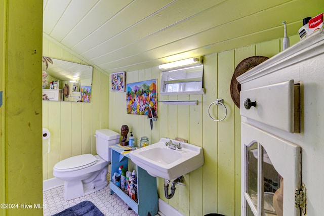 bathroom featuring lofted ceiling, tile patterned floors, toilet, sink, and wood walls