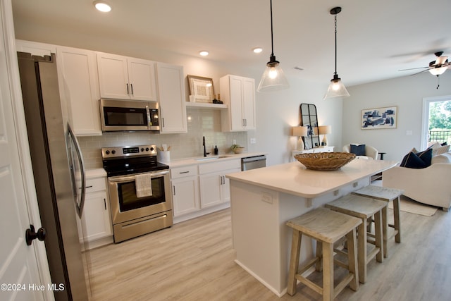 kitchen with stainless steel appliances, a sink, backsplash, light wood-style floors, and a breakfast bar