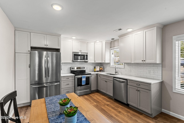 kitchen with stainless steel appliances, gray cabinetry, backsplash, dark wood-type flooring, and sink