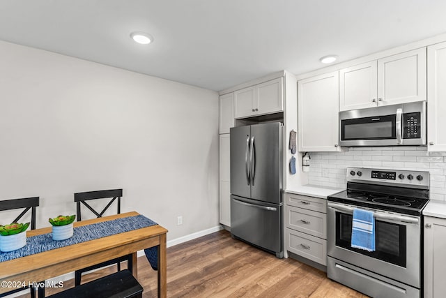 kitchen with backsplash, appliances with stainless steel finishes, white cabinetry, and light hardwood / wood-style flooring