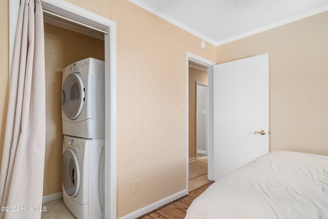 laundry room with stacked washing maching and dryer, light wood-type flooring, ornamental molding, and a textured ceiling