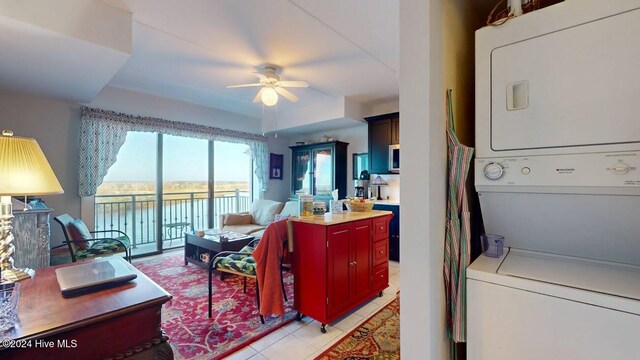 tiled living room with stacked washing maching and dryer, a water view, and ceiling fan