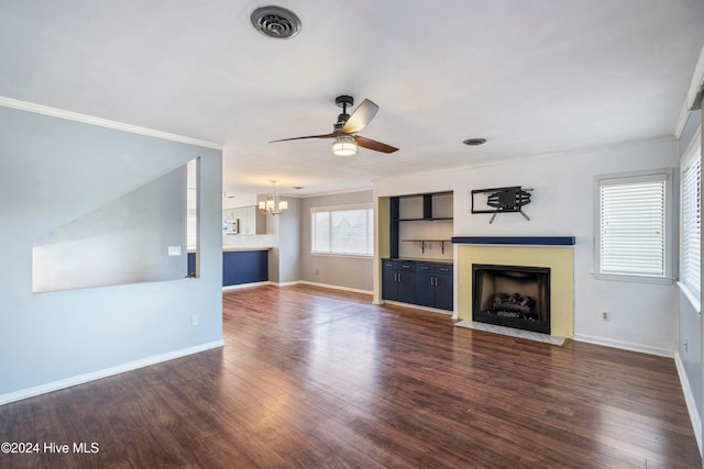 unfurnished living room featuring dark wood-type flooring, ornamental molding, and ceiling fan with notable chandelier