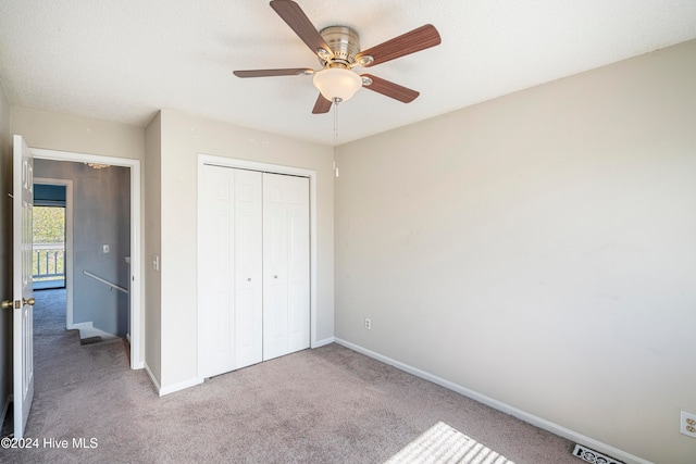 unfurnished bedroom featuring a closet, ceiling fan, a textured ceiling, and light colored carpet