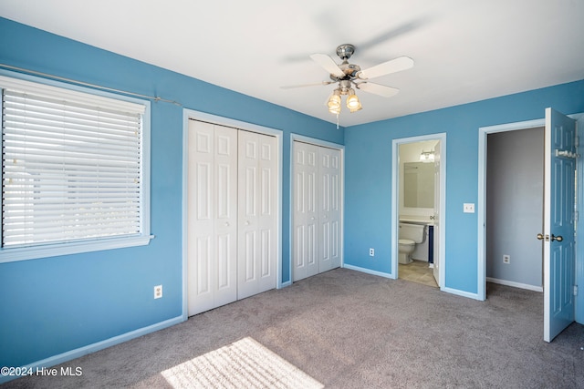 unfurnished bedroom with two closets, ceiling fan, light colored carpet, and ensuite bath