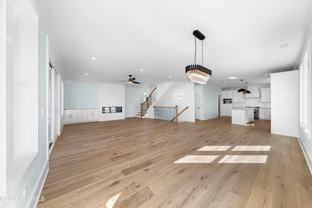 unfurnished living room featuring ceiling fan with notable chandelier and light wood-type flooring