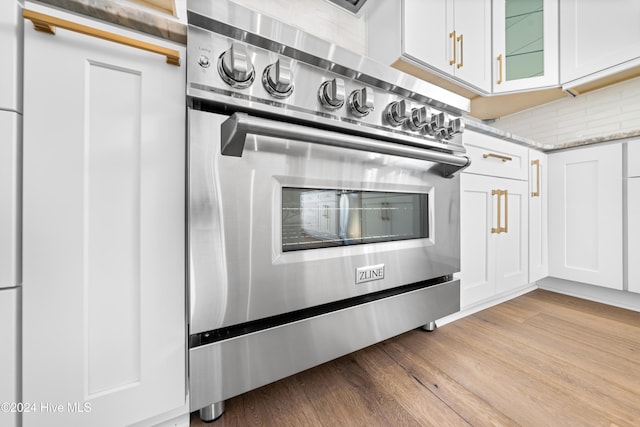 kitchen with white cabinets, backsplash, light stone countertops, light hardwood / wood-style floors, and stainless steel double oven