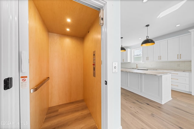 interior space featuring elevator, hanging light fixtures, light stone countertops, light wood-type flooring, and white cabinetry