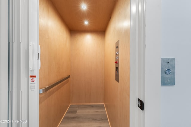 interior details featuring hardwood / wood-style floors, elevator, and wooden walls