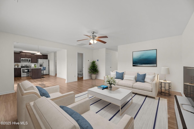 living area featuring visible vents, baseboards, light wood-style flooring, and a ceiling fan