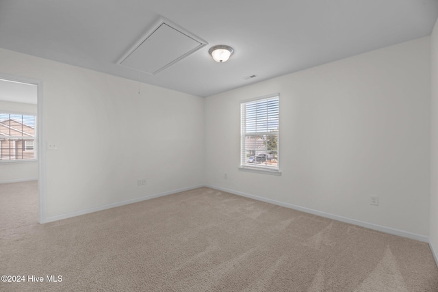 spare room featuring attic access, plenty of natural light, and light colored carpet