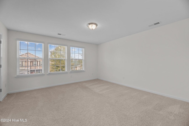 spare room featuring baseboards, visible vents, and light carpet