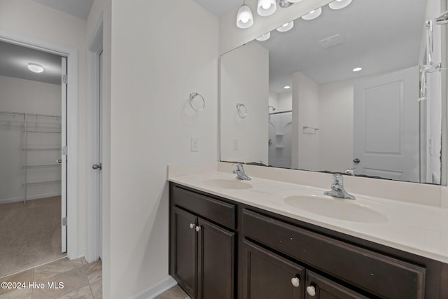 full bathroom with a walk in closet, double vanity, baseboards, and a sink