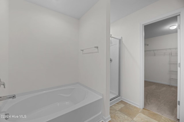 bathroom featuring a shower stall, a spacious closet, a bath, and baseboards