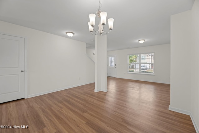 unfurnished living room featuring baseboards, an inviting chandelier, and wood finished floors