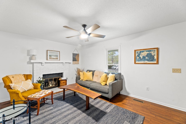 living room with a brick fireplace, a textured ceiling, wood-type flooring, and ceiling fan