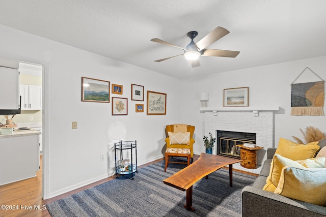 living area featuring a fireplace, ceiling fan, and light hardwood / wood-style flooring