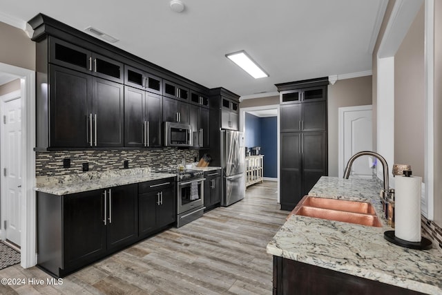 kitchen with crown molding, stainless steel appliances, backsplash, sink, and light hardwood / wood-style flooring