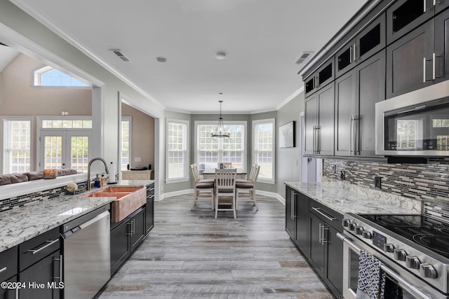 kitchen with light stone counters, appliances with stainless steel finishes, decorative light fixtures, sink, and light hardwood / wood-style flooring