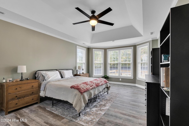 bedroom with a tray ceiling, wood-type flooring, ceiling fan, and crown molding