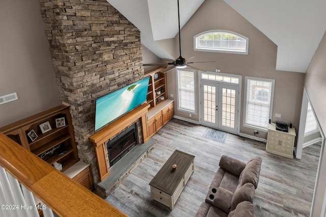 living room with french doors, a stone fireplace, high vaulted ceiling, ceiling fan, and light hardwood / wood-style flooring