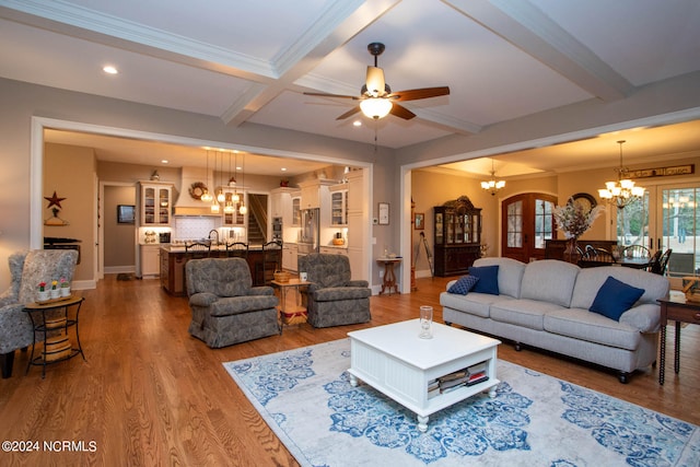 living room with coffered ceiling, beamed ceiling, hardwood / wood-style flooring, ceiling fan with notable chandelier, and ornamental molding