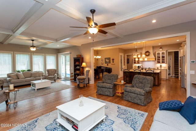 living room featuring ornamental molding, coffered ceiling, ceiling fan with notable chandelier, beam ceiling, and hardwood / wood-style floors