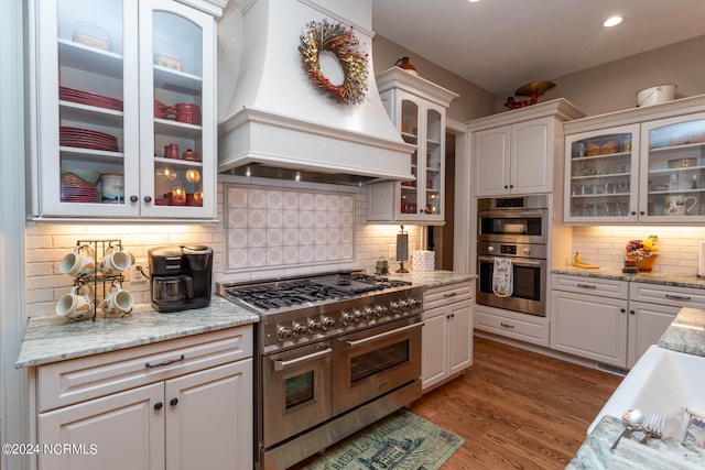 kitchen with decorative backsplash, appliances with stainless steel finishes, white cabinetry, and custom exhaust hood