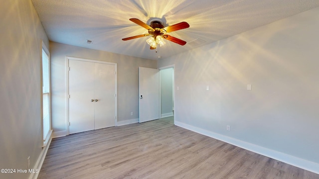 unfurnished bedroom with a textured ceiling, a closet, light hardwood / wood-style floors, and ceiling fan