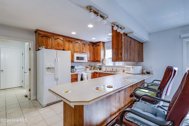 kitchen featuring white appliances, a kitchen bar, light tile patterned floors, sink, and kitchen peninsula