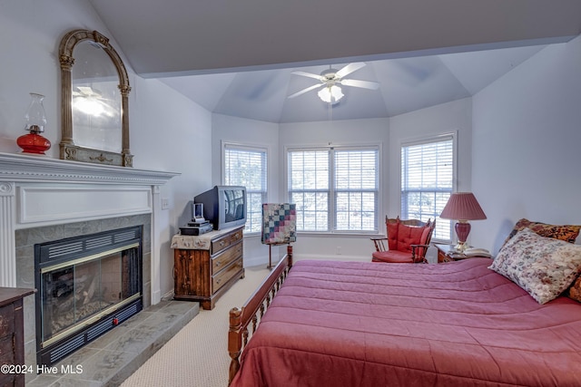 carpeted bedroom featuring ceiling fan, a tile fireplace, and vaulted ceiling